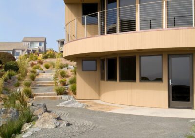 Modern curved house with expansive windows overlooking a landscaped garden with rocks and shrubs.