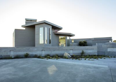 Modern single-story house with expansive windows and a flat roof, featuring stone accents in a desert landscape.