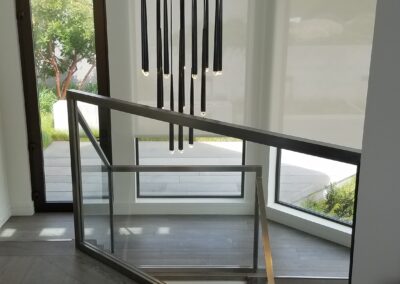 A modern staircase with glass railings and a hanging chandelier in a contemporary home interior.