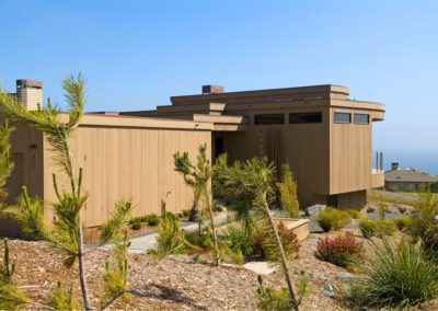 Modern hillside house with ocean view surrounded by native vegetation.