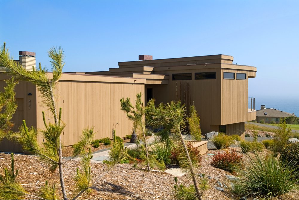 Modern hillside home with ocean view and native vegetation.