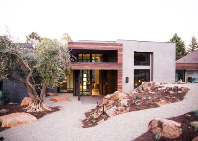Modern house with large windows amid landscaped grounds at dusk.