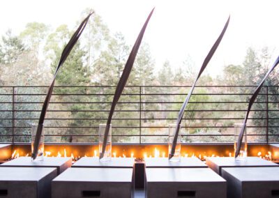 Outdoor seating area with a modern fire feature against a railing overlooking a natural backdrop.