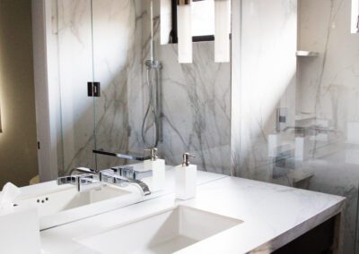 A modern bathroom with marble walls, a double sink vanity, and hanging pendant lights.