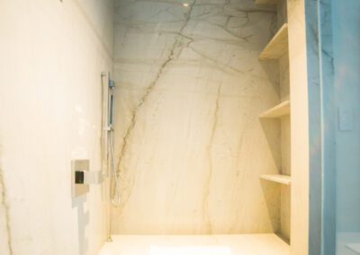 Marble tiled walk-in shower with built-in bench and shelving.