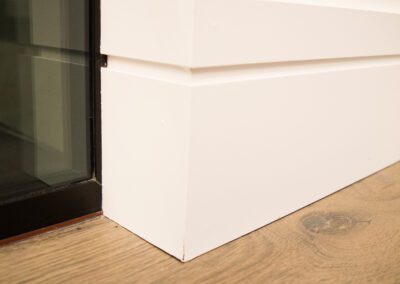 White skirting board meeting at a corner on a wooden floor beside a glass pane.