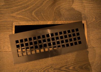 A floor vent grille partially opened on a wooden floor.