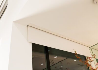 Interior corner of a room showing a white ceiling and wall with a recessed light and a view of a glass panel.