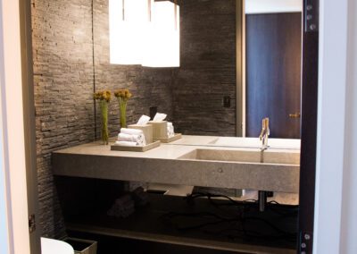 Modern bathroom interior featuring dark textured walls, wood-effect flooring, a rectangular basin, and a minimalist light fixture.