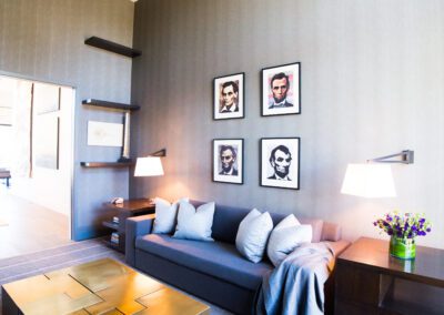 Modern living room with a gray sofa, metallic coffee table, and a gallery wall of framed portraits.