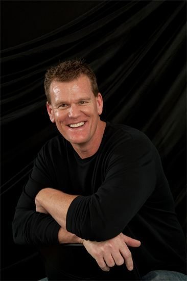 Smiling man with crossed arms against a black background.